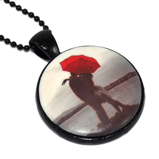Μενταγιόν σε μαύρη στρογγυλή απλή βάση με ζευγάρι που φιλιέται κάτω από κόκκινη ομπρέλα