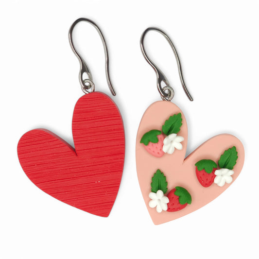 Κρεμαστά σκουλαρίκια ανόμοιες καρδιές κόκκινες φραουλίτσες σε απαλό ροζ φόντο από πολυμερικό πηλό