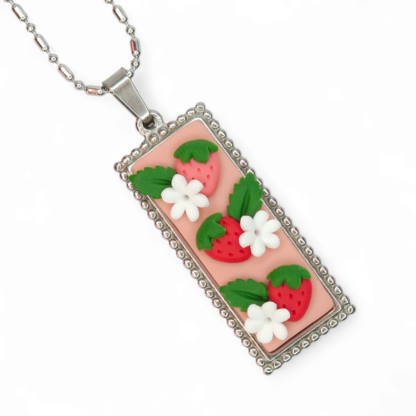 Μακρύ ατσάλινο κολιέ με κόκκινες φραουλίτσες σε απαλό ροζ φόντο από πολυμερικό πηλό